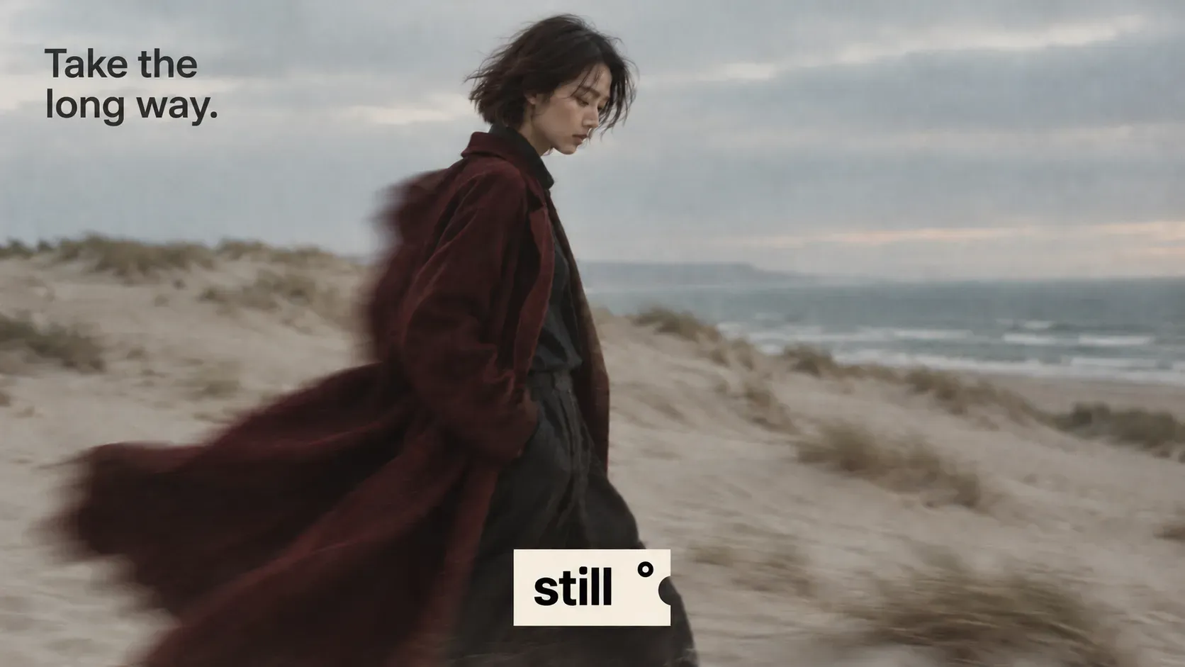 Take the long way campaign visual with a woman in a red coat on windy dunes
