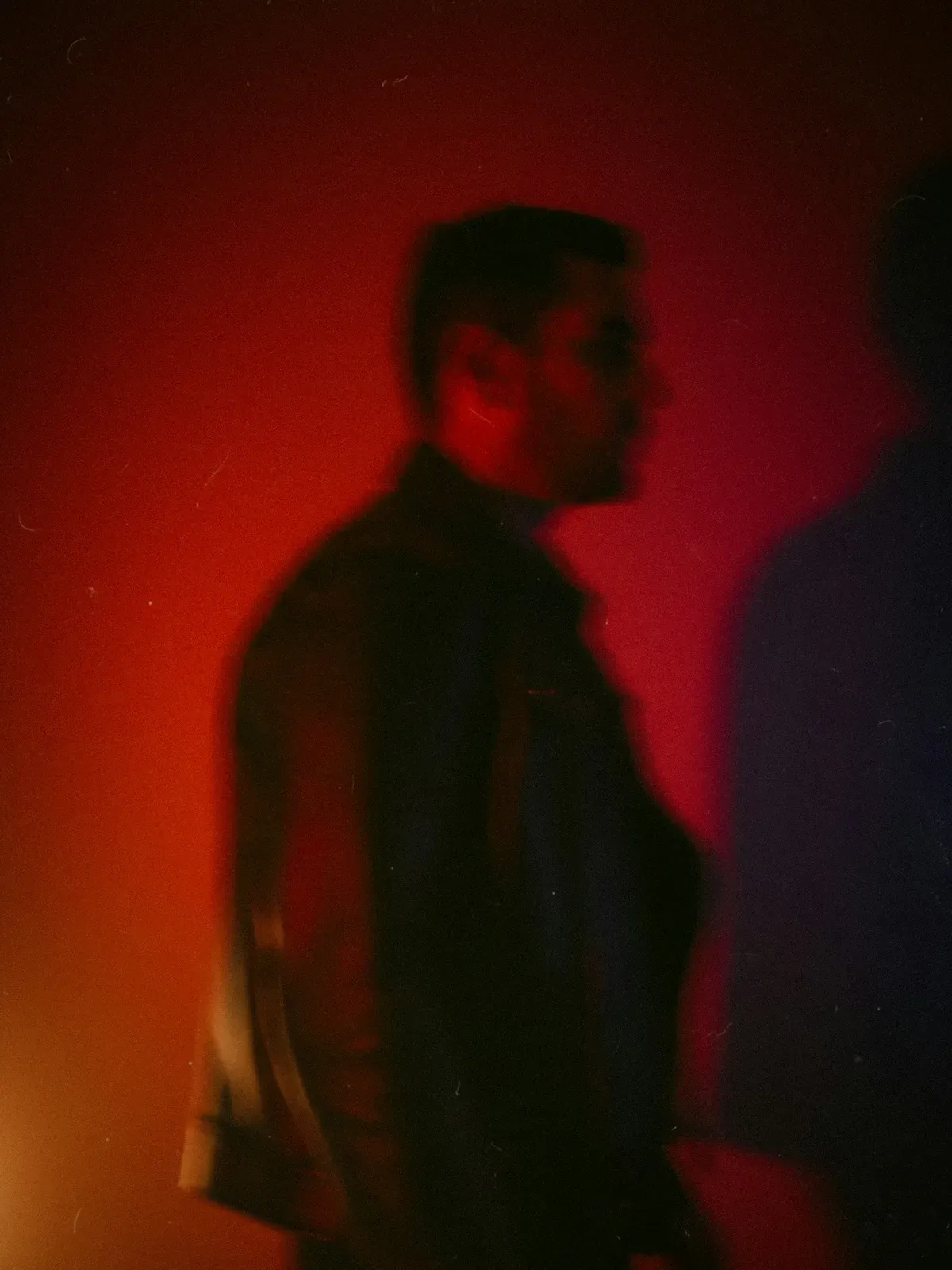 A man in profile, half in shadow, against a deep red wall