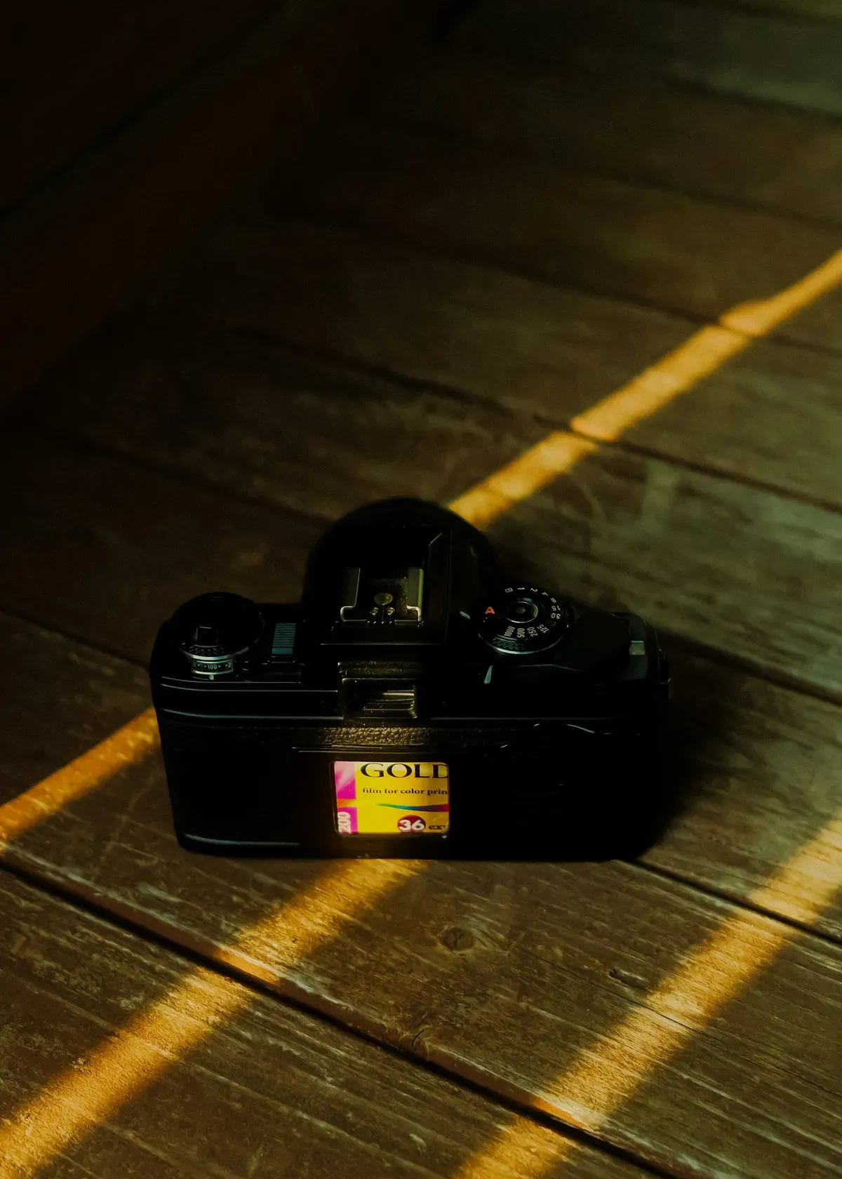 A film camera on a wooden floor crossed by streaks of warm sunlight